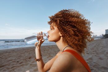 Soif d'été : Femme heureuse buvant de l'eau sur une plage ensoleillée, profitant de ses vacances