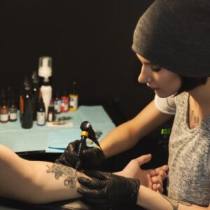 Young Woman Tattooist Doing Tattoo On Male Arm