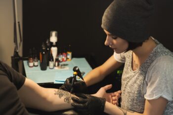 Young Woman Tattooist Doing Tattoo On Male Arm