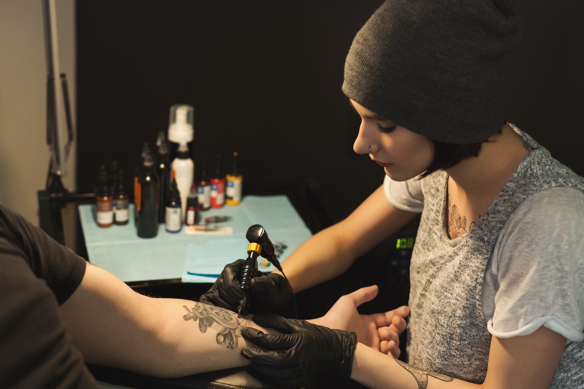 Young Woman Tattooist Doing Tattoo On Male Arm